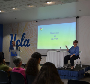 The image shows Donalda Ammons and Professor Benjamin Lewis on stage, a slide with a blue-green gradient slide and "Questions and Answers" text, as well as some members from the audience.